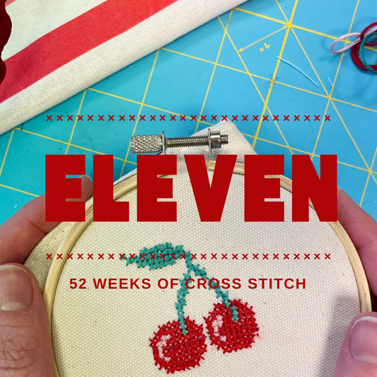 cross stitch hoop with red cross-stitched cherries with a blue grid background.