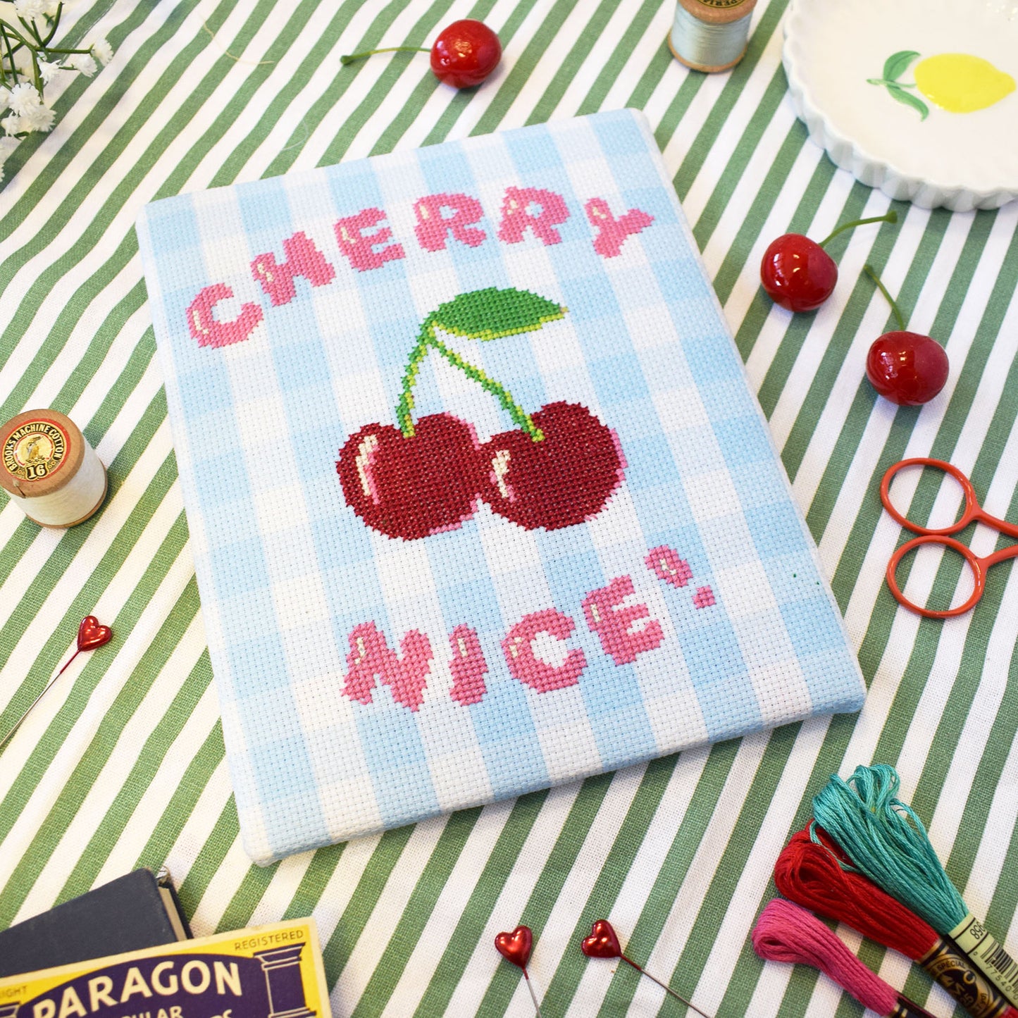 cross stitch design on blue gingham aida. The design is has the motif cherry nice with a large red cherry motif.