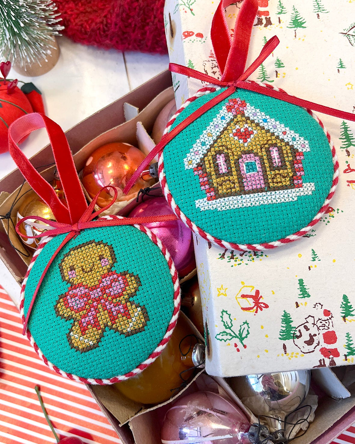 Cross-stitched Christmas ornaments with gingerbread design on a box of Christmas decorations.