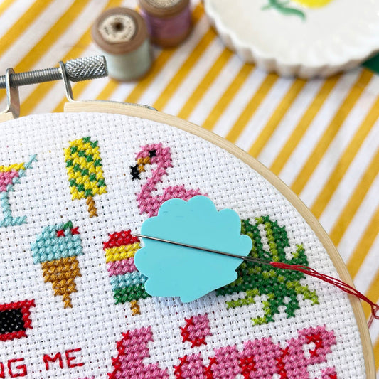 mint green coloured shell shaped acrylic needle minder on a sunshine themed cross stitch hoop.