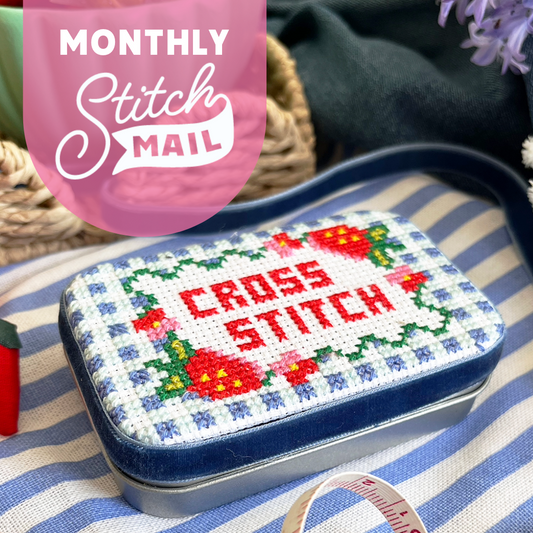 Cross-stitched tin with 'Cross Stitch' text on a striped fabric background, featuring 'Monthly Stitch Mail' branding.