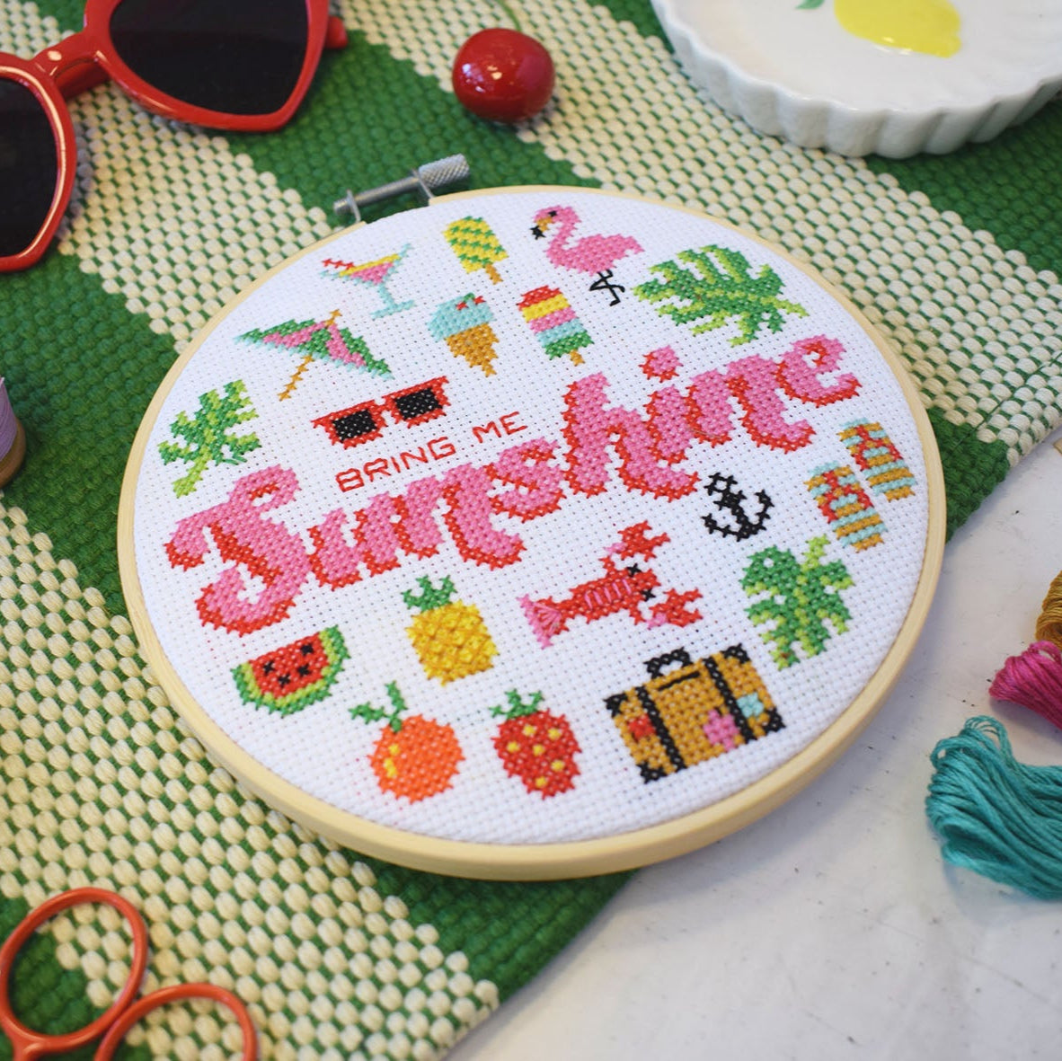 Bring Me Sunshine cross stitch kit with 6-inch hoop, colourful threads, Aida fabric on a green stripy background and heart shaped sunglasses