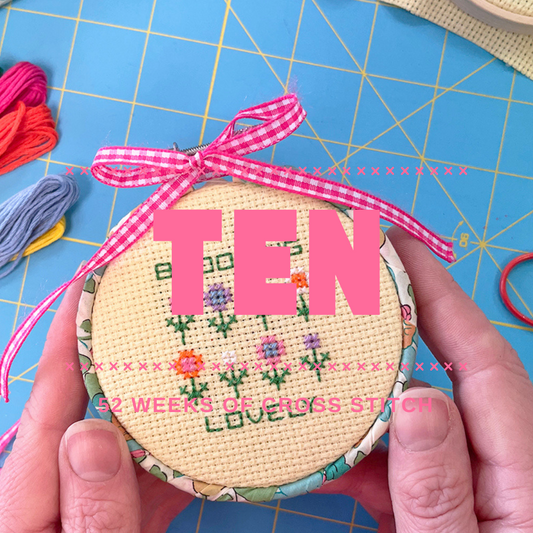 Handmade cross sttich kit with and floral patterns, held by hands on a blue cutting mat.