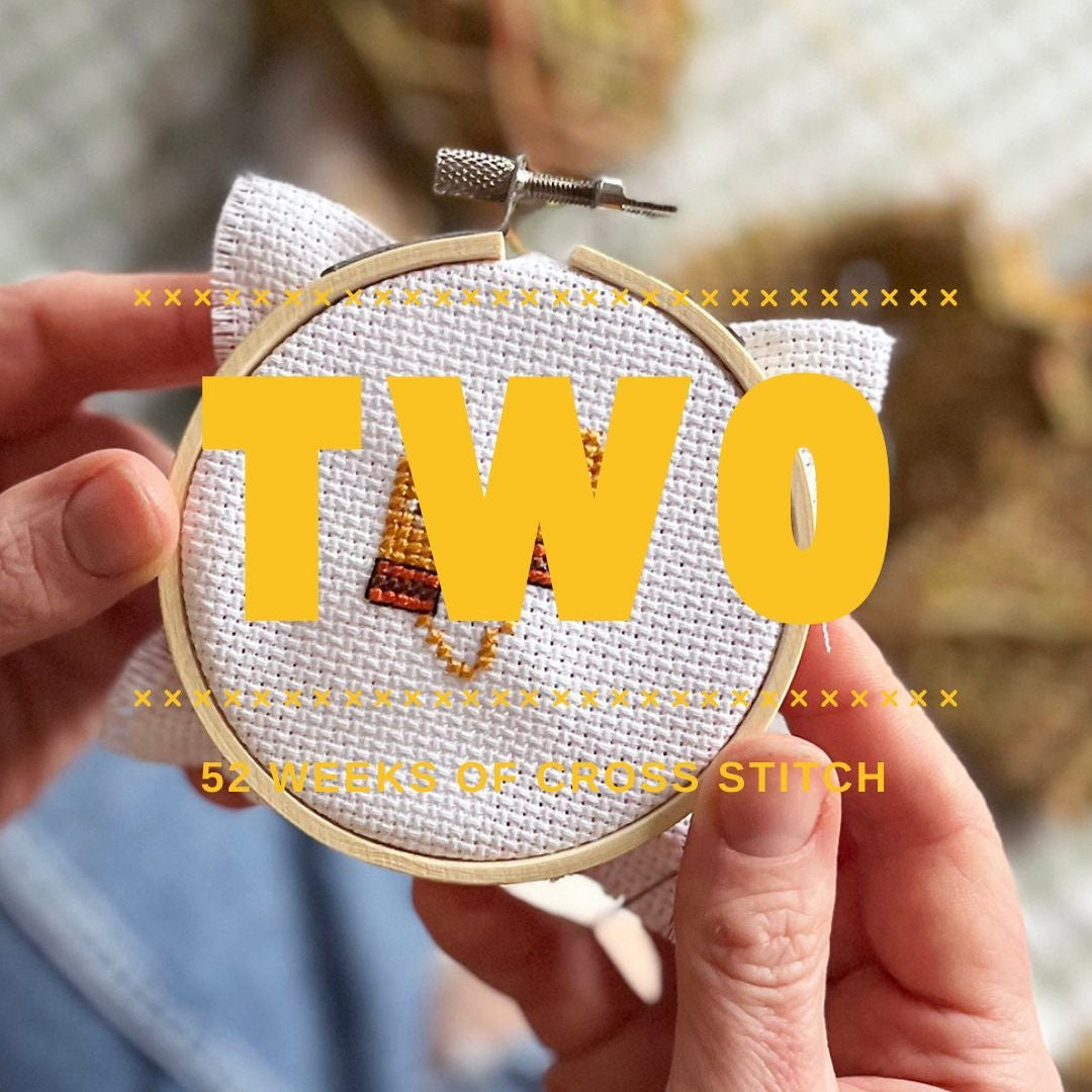 Hand holding a small embroidery hoop with 'TWO' in yellow letters, blurred background