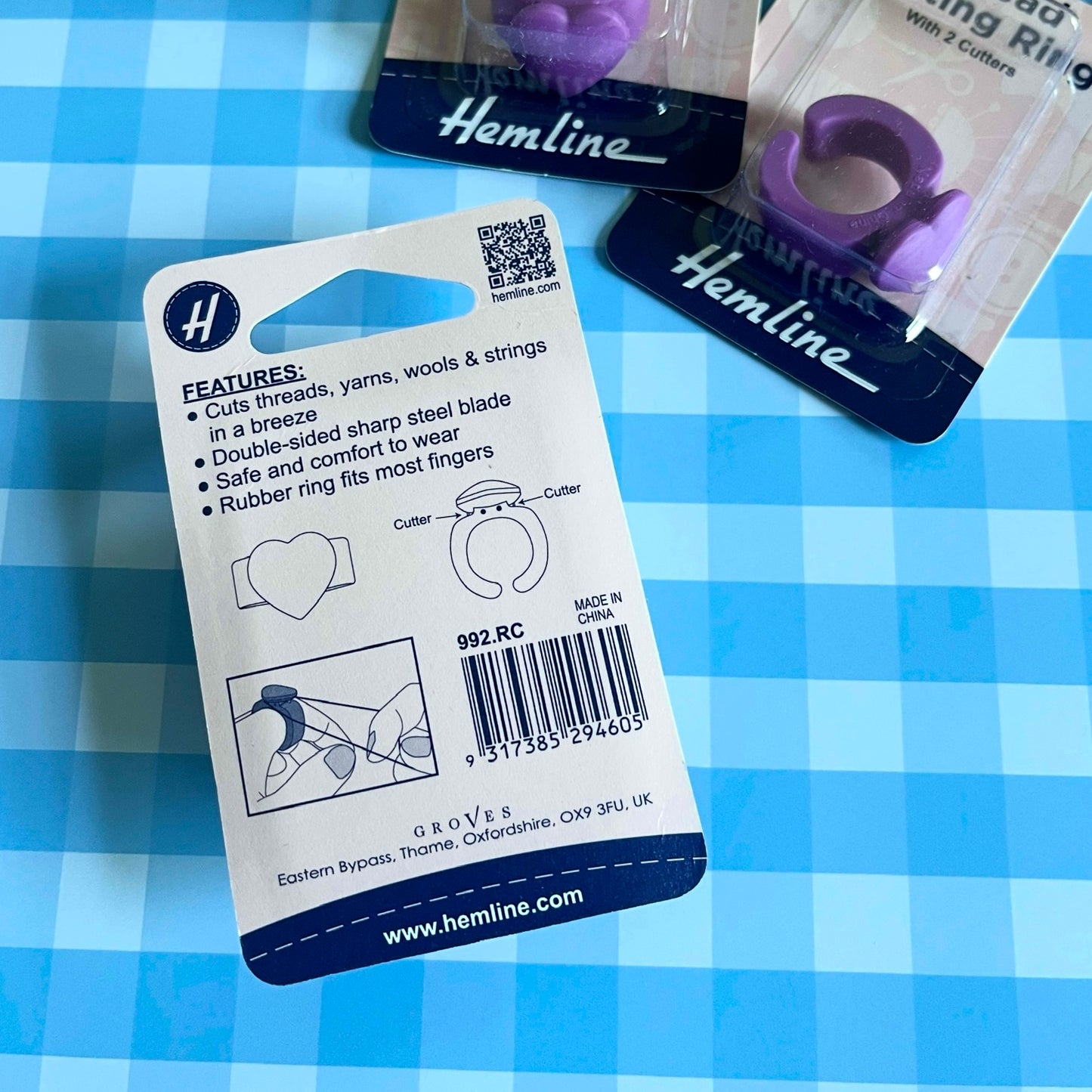 Packaged purple rubber ring finger cutter by Hemline on a blue and white checkered background, with the back of the retail card visible and two additional packaged units partially shown.