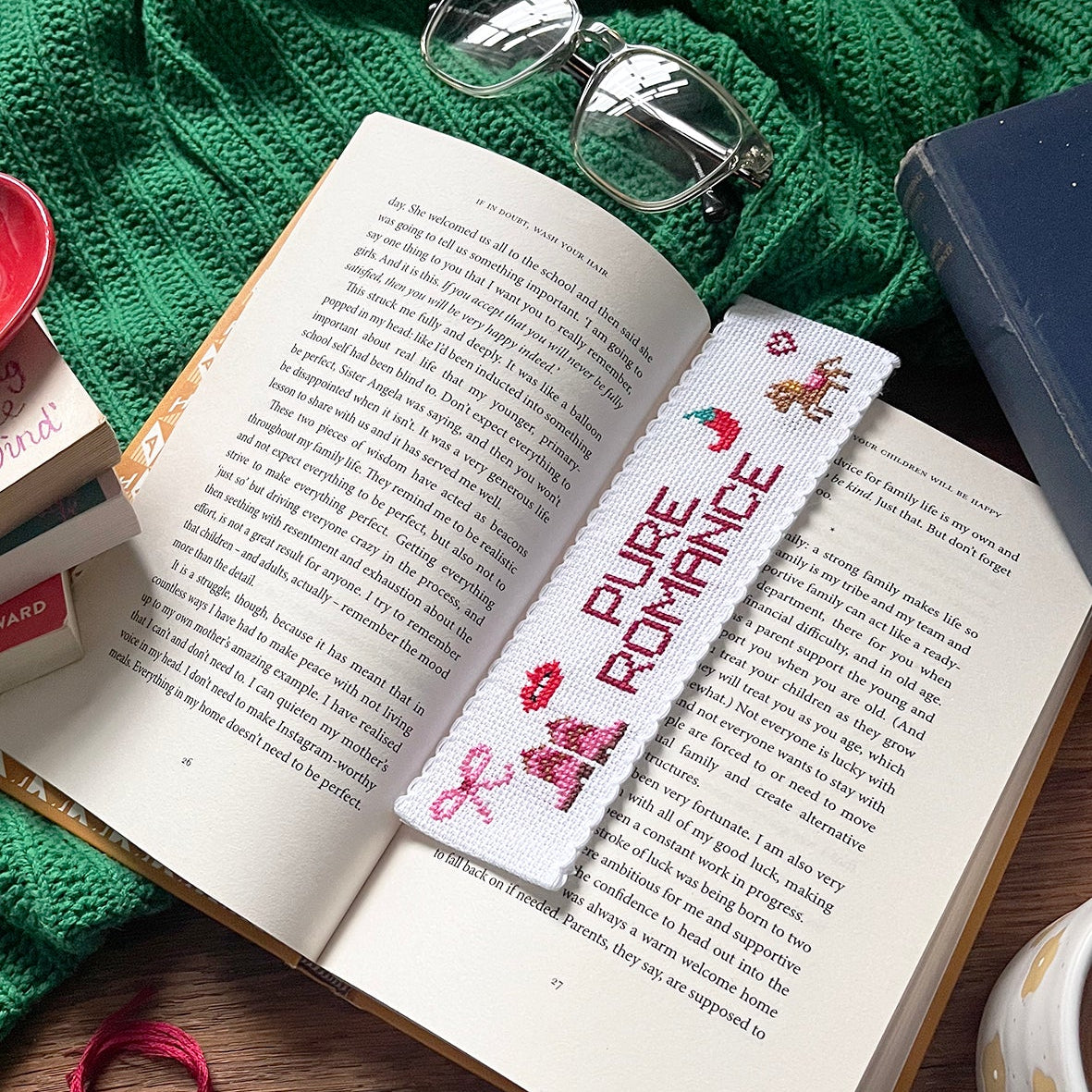 Open book with a 'PURE ROMANCE' bookmark on a wooden surface with green fabric and small containers.