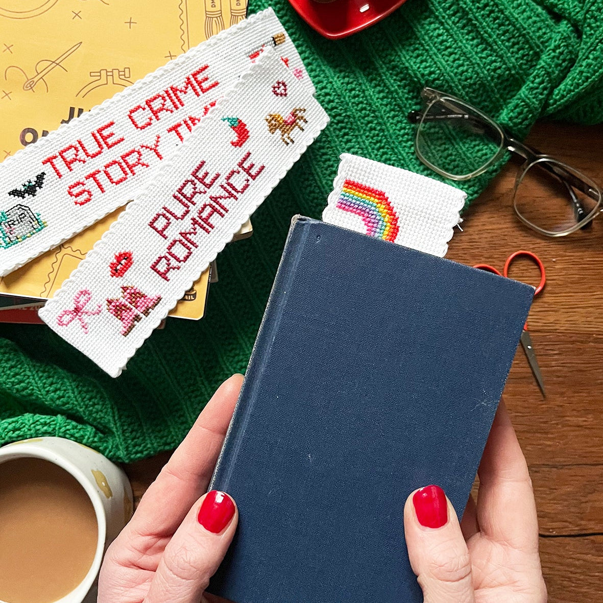 Person holding a blue notebook with cross-stitched bookmarks on a cozy background
