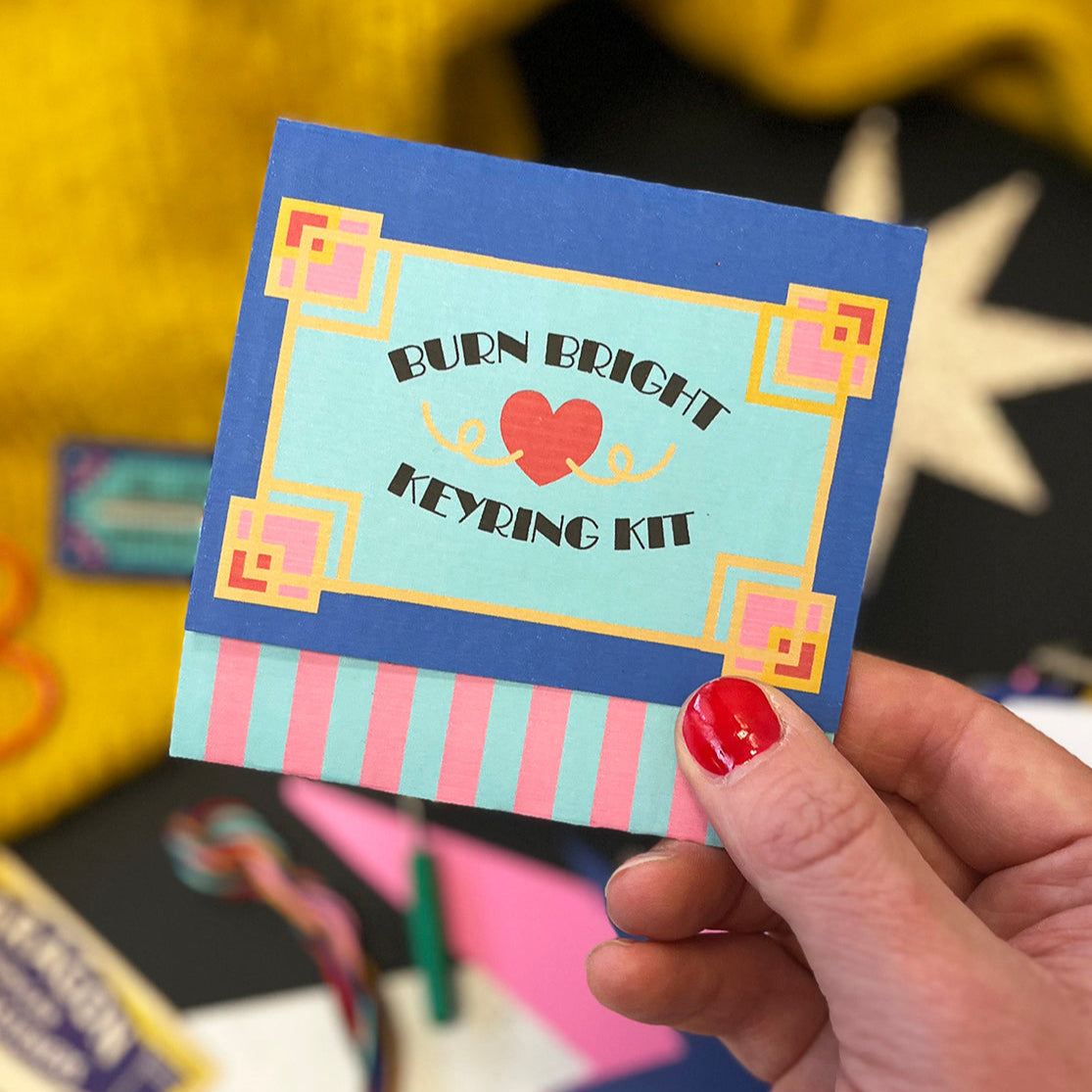 Hand holding a colorful keyring kit packaging with text on a blurred background