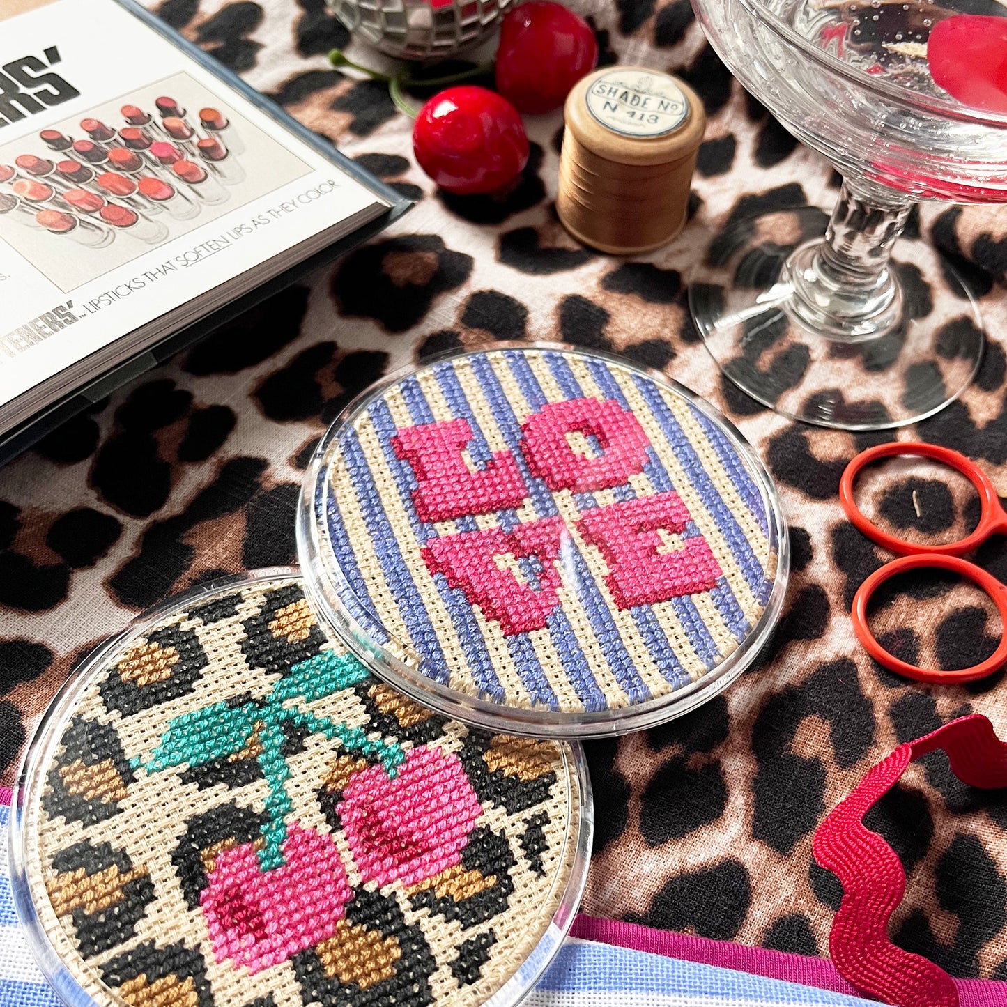 Two decorative coasters on a leopard print surface with a disco ball, red berries, and a magazine.