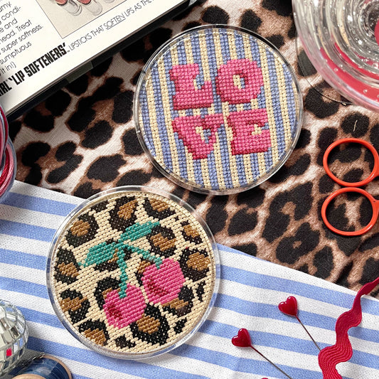 Two decorative coasters with 'LOVE' and leopard print design on a patterned surface.