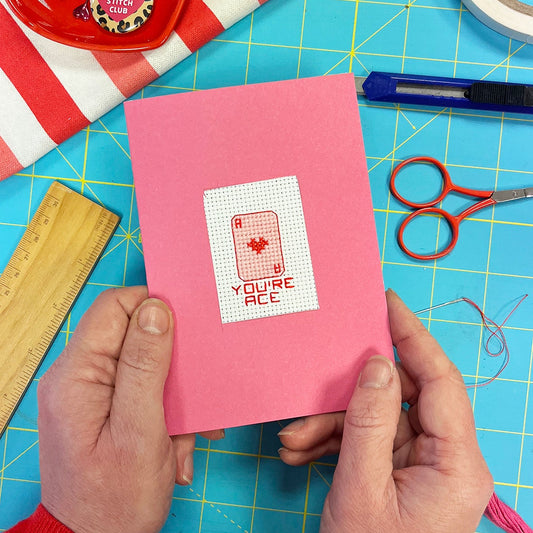 pink valentines card with a cut out section with a cross stitch design with a ace of hearts card with 'you're ace' underneath it.