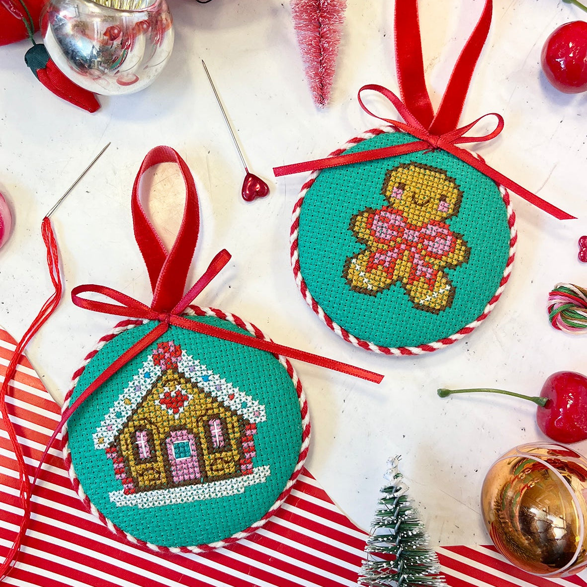 Two cross-stitched Christmas ornaments with gingerbread and house designs on a festive background.
