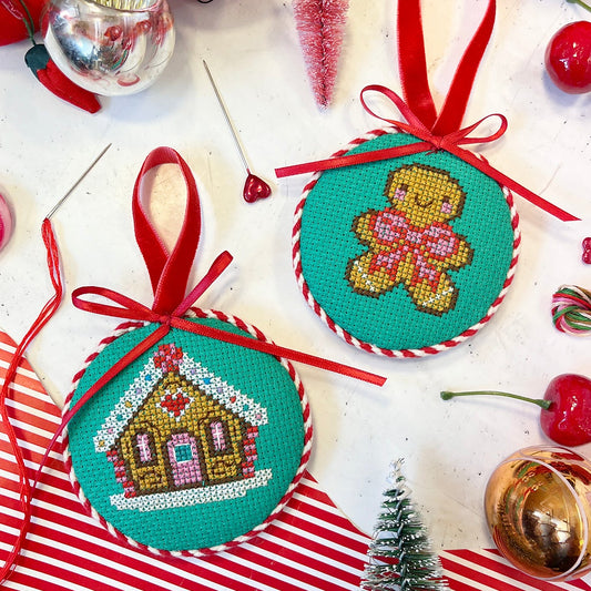 Two cross-stitched Christmas ornaments with gingerbread and house designs on a festive background.