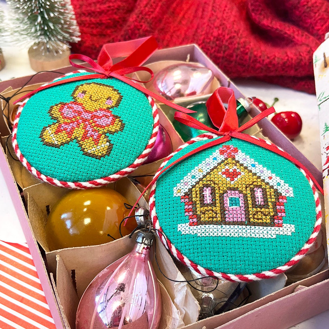 Decorative Christmas ornaments in a box with gingerbread designs on a red and white striped surface.