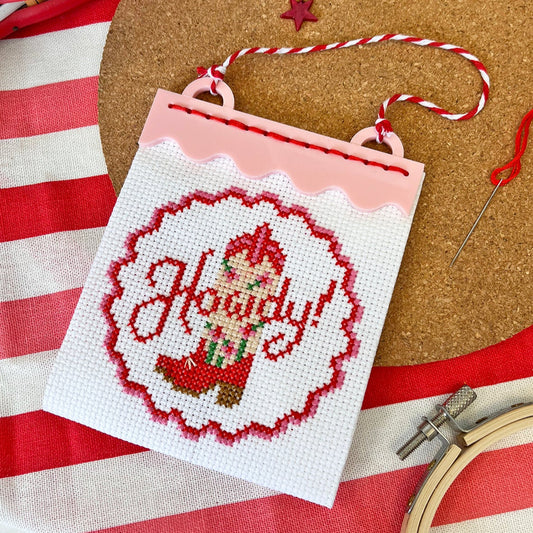 Cross-stitched ornament with 'Howdy!' design on a red and white striped fabric background.