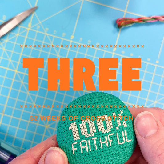 a blue background with some hands holding a green cross stitched magnet with the slogan 100% Faithful on it.