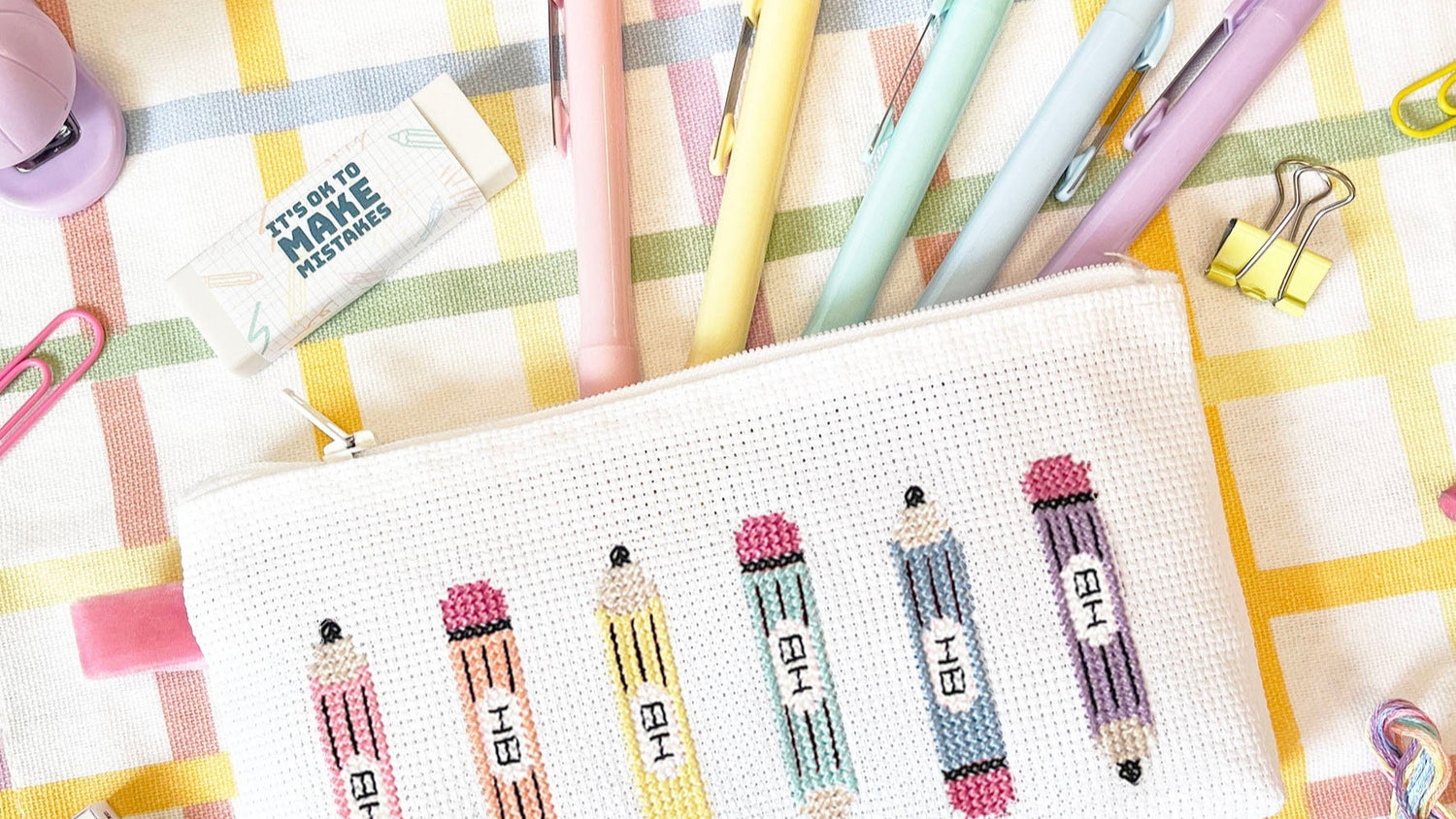 pencil case with cross stitch pencil with a Set of pastel-coloured stationery items on a checkered surface