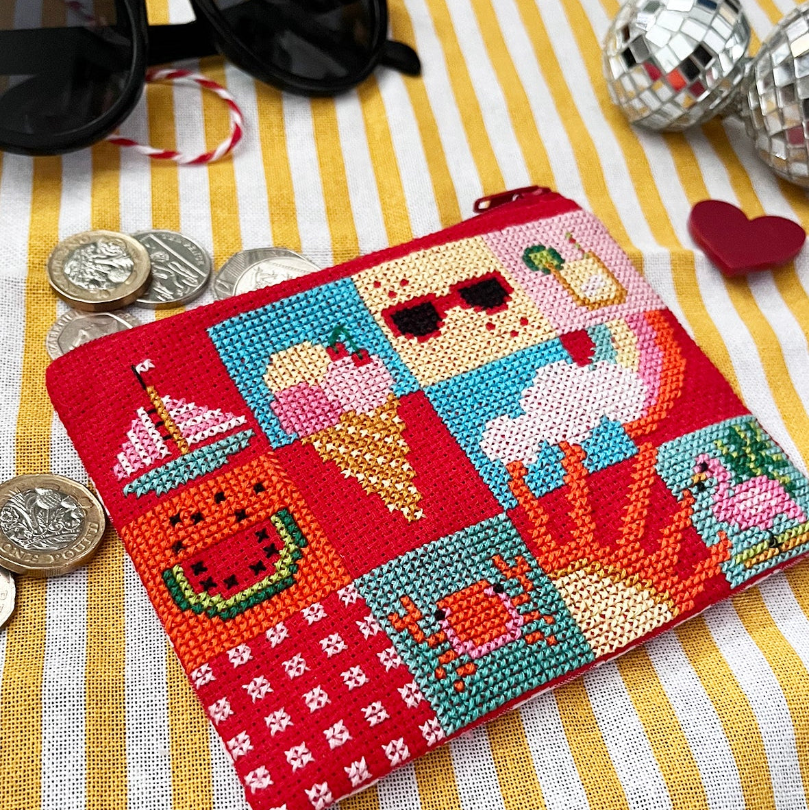 Cross-stitched cross stitch purse with colourful designs on a yellow striped fabric background.