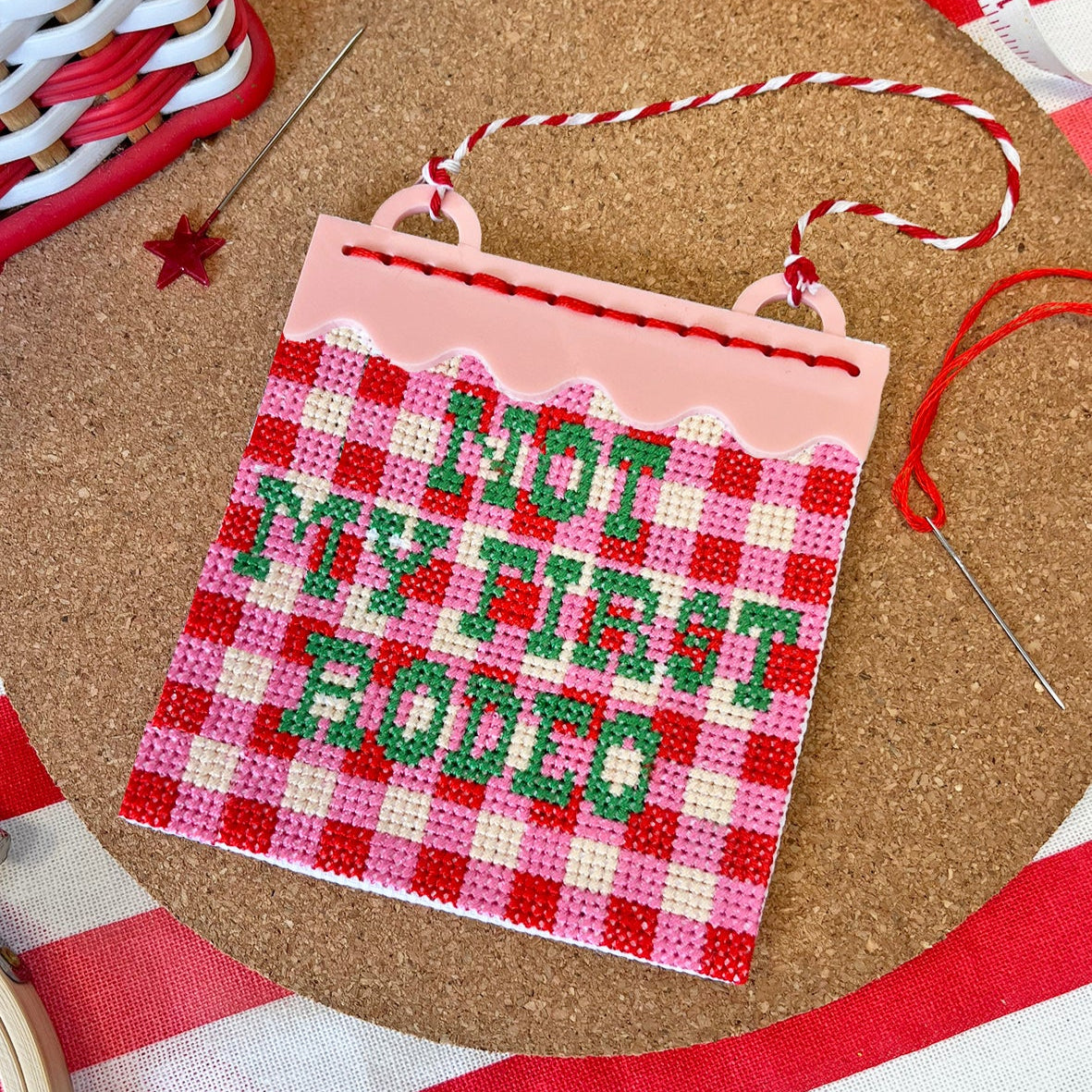 Cross-stitched sign with 'not my first rodeo' text on a red and white striped surface