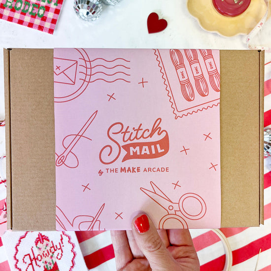 Stitch Mail box held by a hand on a red and white striped background with decorative items.