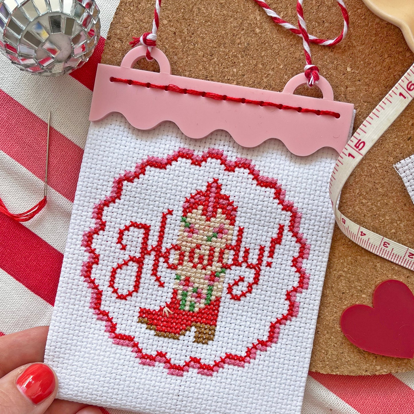 Cross-stitched ornament with 'Howdy' design held by a hand on a festive background.